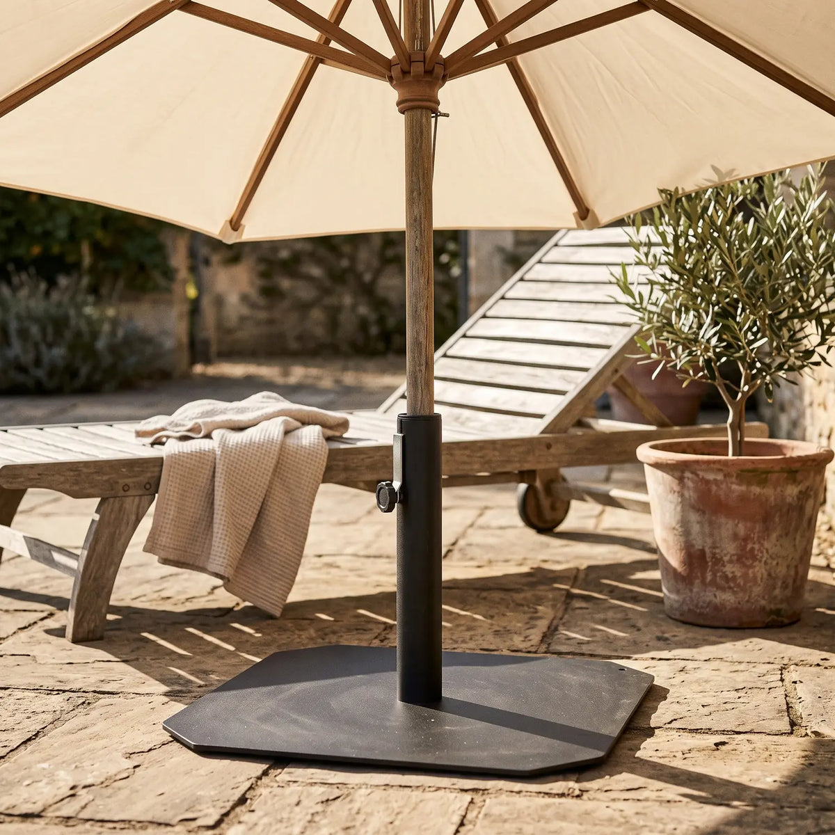 Square Parasol Base in black iron holding a parasol pole on a stone terrace