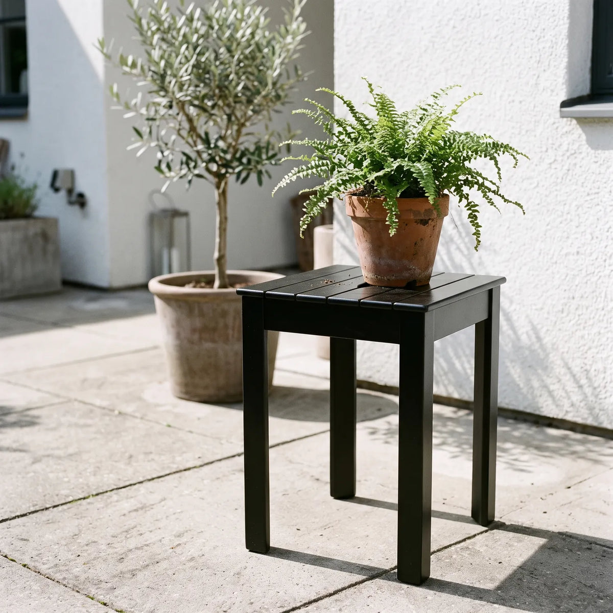 Tokyo Stackable Stool in Black with a fern on a modern courtyard patio